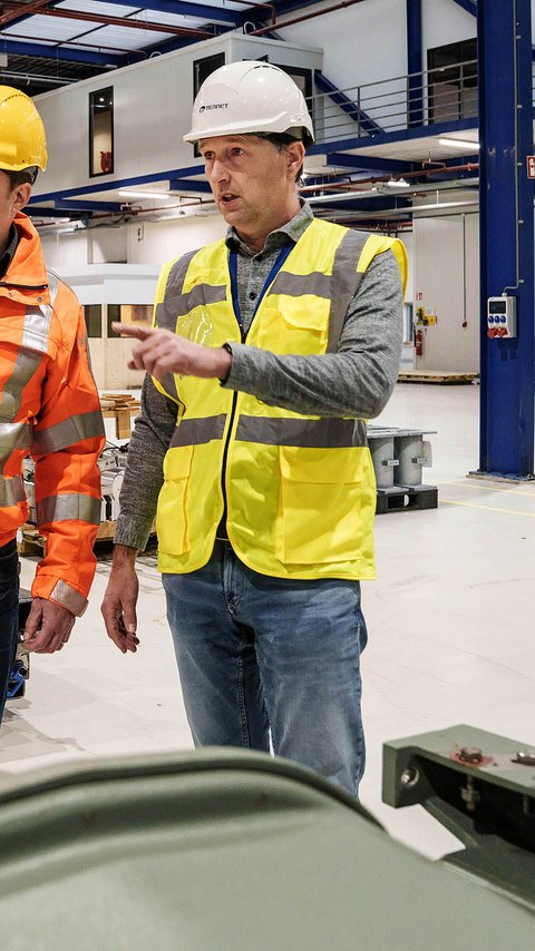 Een collega van Heijmans en een collega van TenneT wijzen in de fabriekshal van de fabriek Krachtvel in Ede.