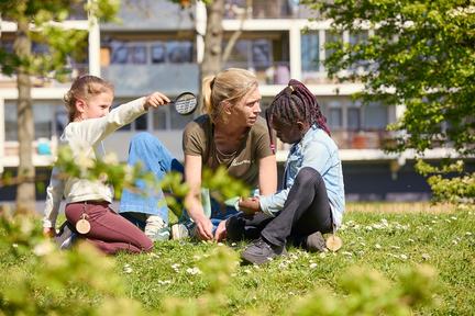 Drie personen zitten op een grasveld voor een flat.
