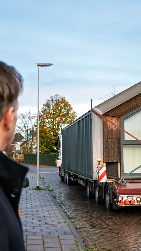 Rechts zie je een vrachtwagen met daarop het bovenste deel van de Heijmans ONE dat verplaatst wordt. Links zie je projectmanager Martijn Ras